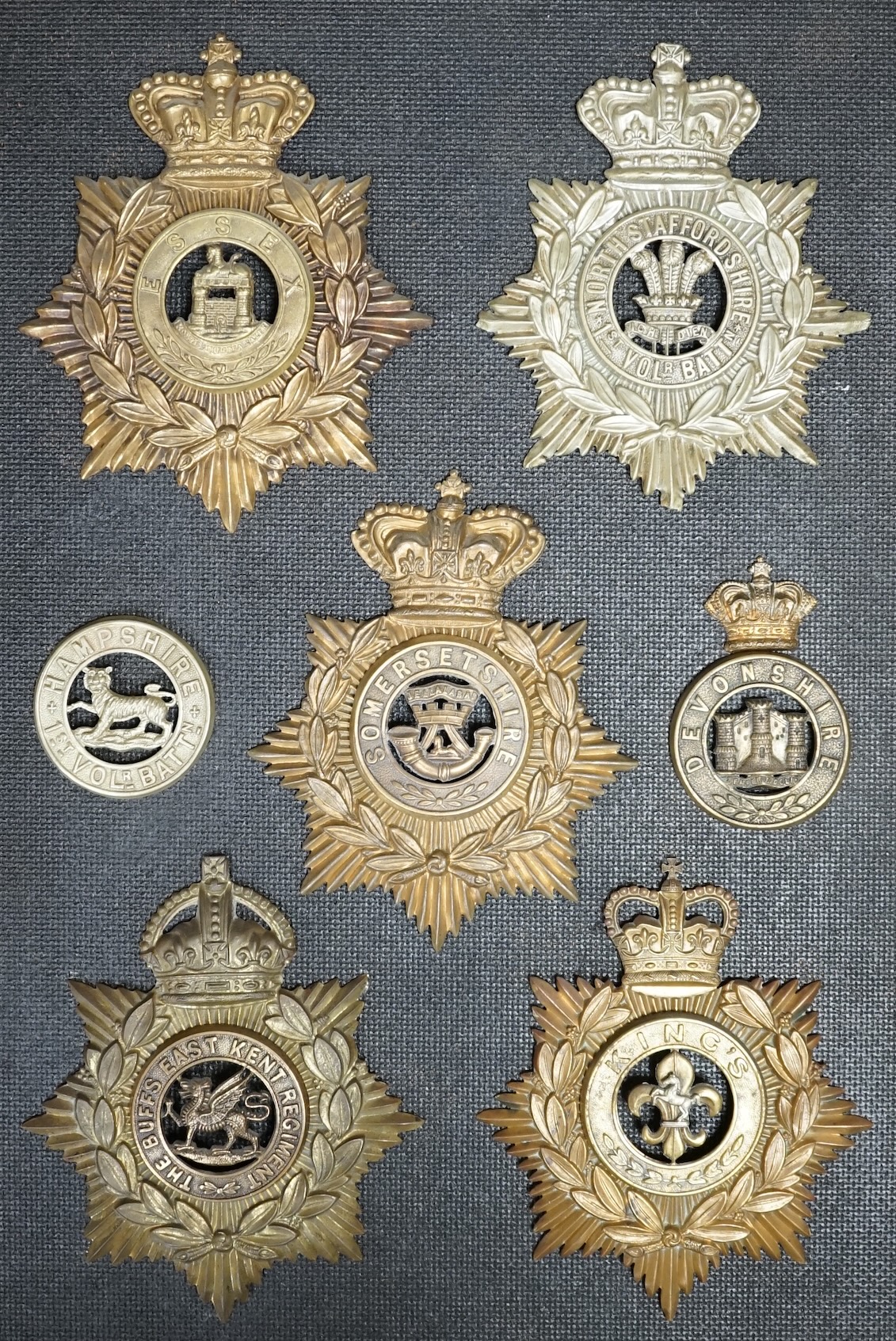 Five military helmet plates and two other centre badges, mounted on a board including; the Essex Regiment, the North Staffordshire 1st Volunteer Battalion, the Somerset Regiment, the Buffs East Kent Regiment, the King’s